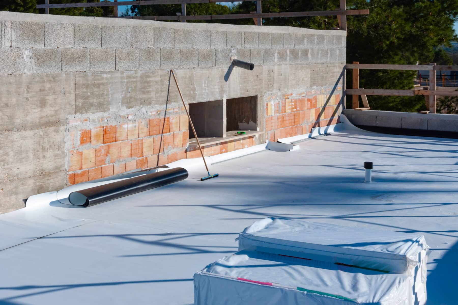 Flat roof under construction with white TPO roofing membrane being installed and tools placed on the surface