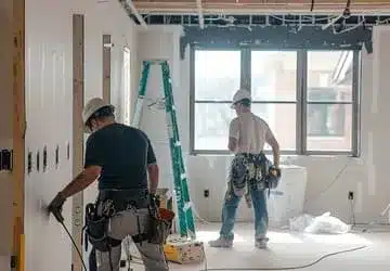 Construction workers installing drywall in a partially finished room