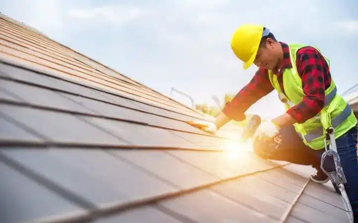 Construction worker in safety gear installing metal roof panels with a hammer