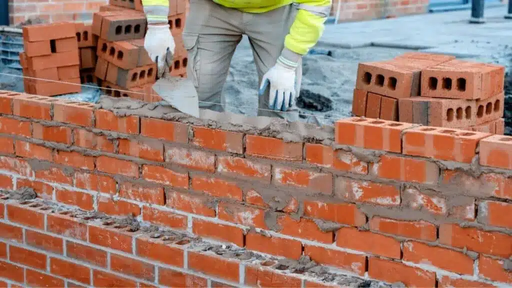 Construction worker laying red bricks and applying mortar to build a brick wall on a residential construction site