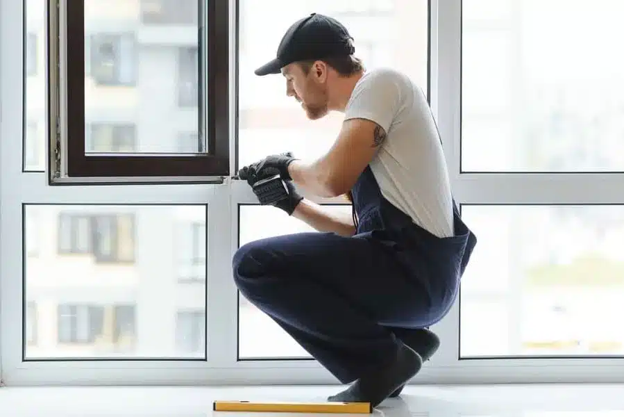Workman in overalls installing or adjusting plastic windows in the living room at home