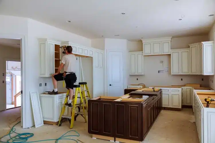 Worker installing upper kitchen cabinets during renovation in East Providence
