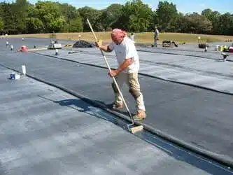 Worker sealing seams on a flat rubber roof (EPDM) with a roller.