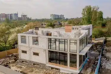 Modern two-story home under construction in Providence using white foam concrete blocks, featuring large glass windows and partially completed brick chimneys.