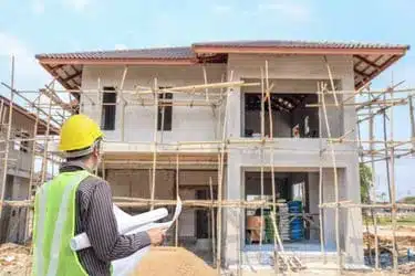 Architect or engineer in safety gear inspecting residential construction in Providence, holding blueprints and reviewing progress on a two-story modern home.