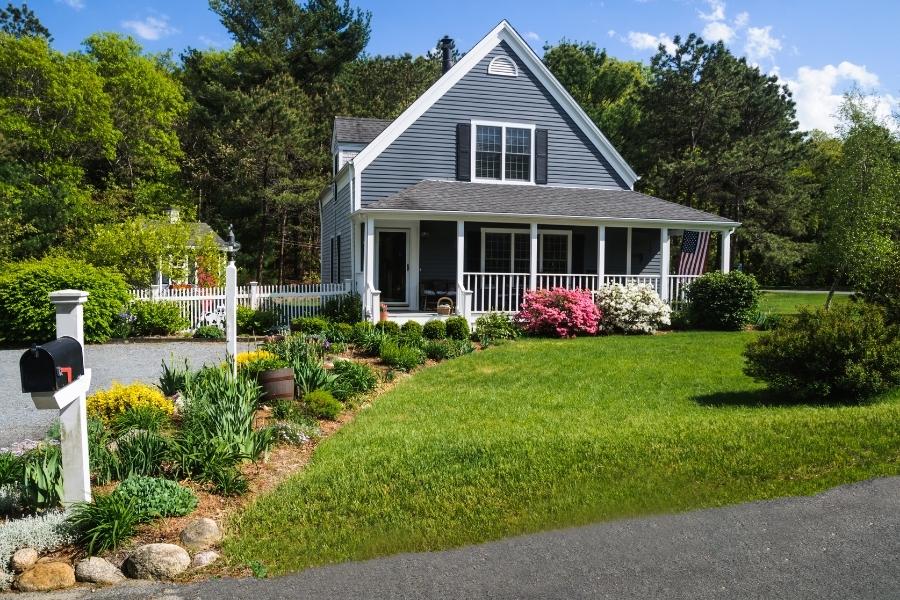 A blue house with a front porch, surrounded by lush greenery and colorful flowers