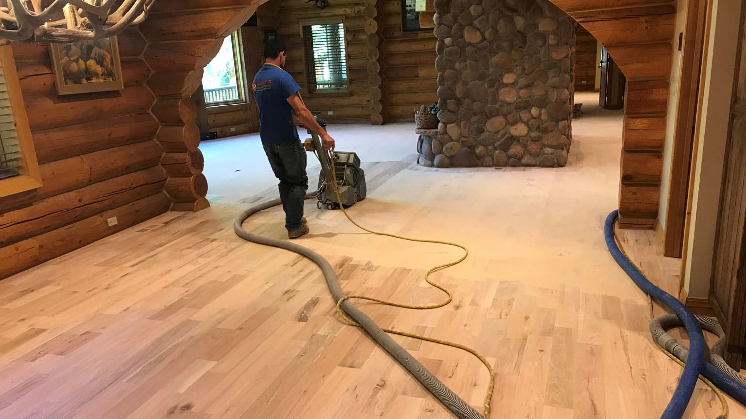 A person sands a wooden floor in a log cabin room.
